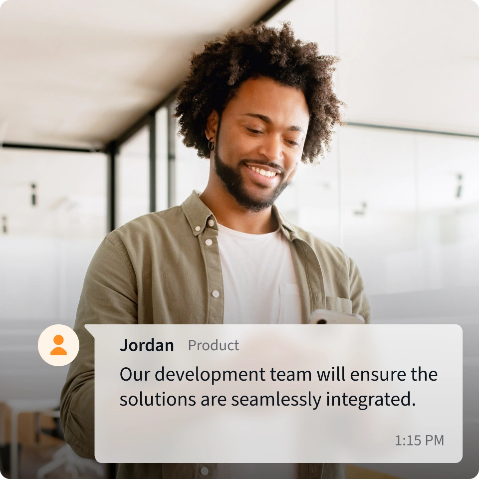A product professional is walking through an open-concept office setting communicating with a partner over a mobile device. 