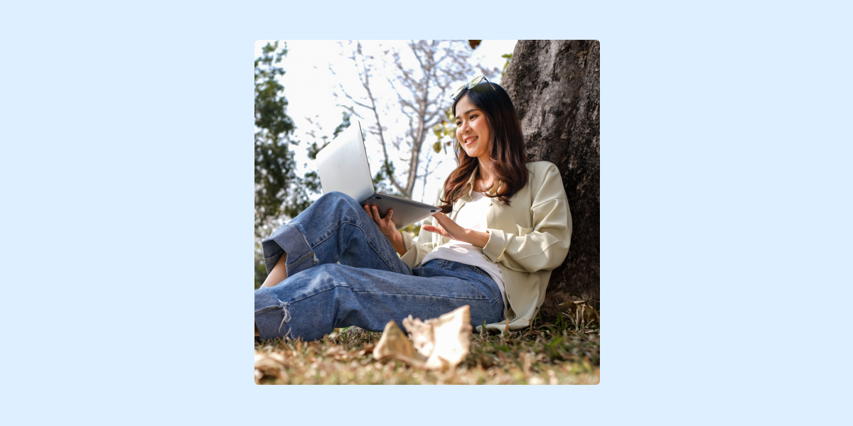 Person sitting outdoors by a tree using a laptop.