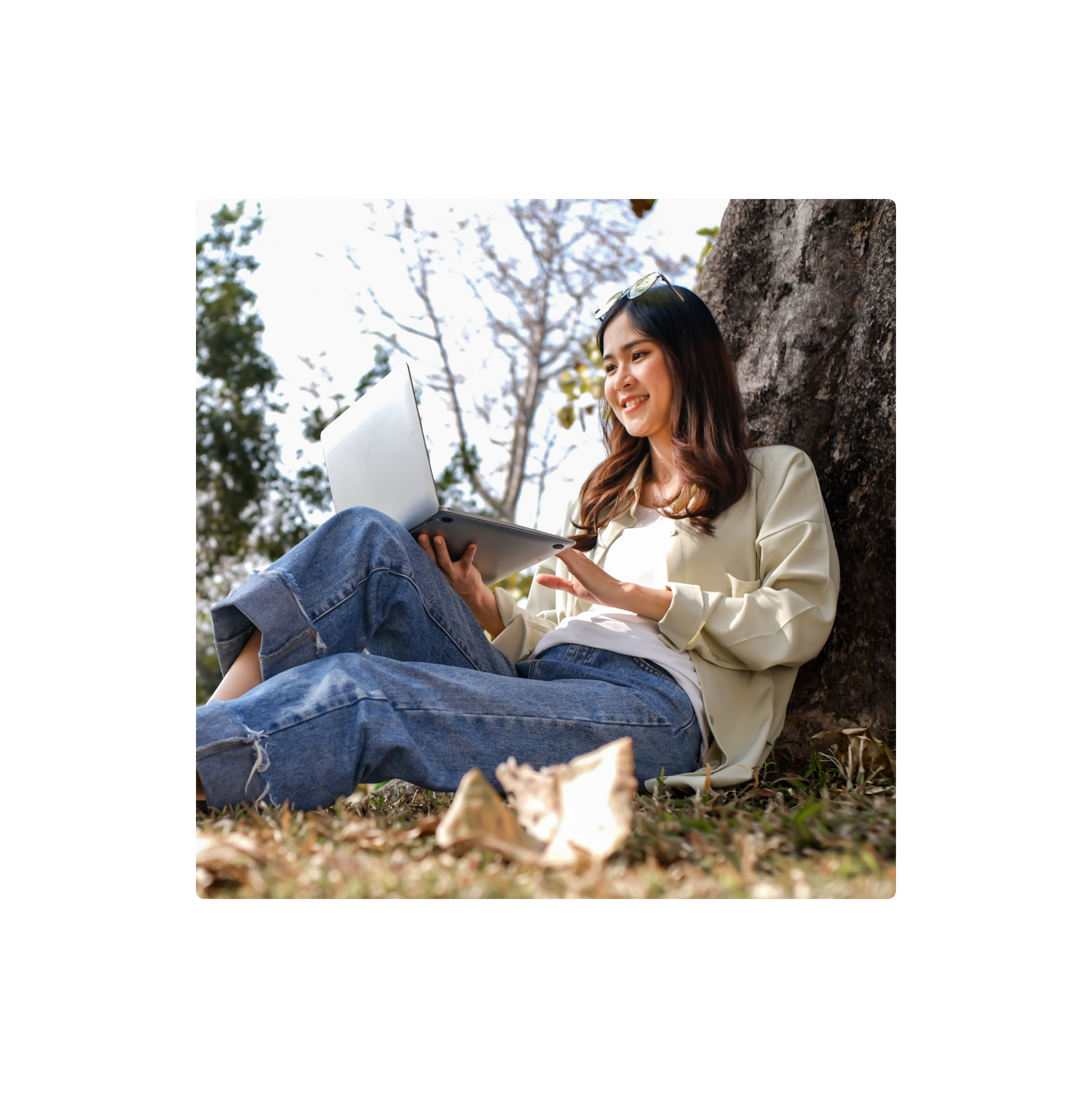 Person sitting outdoors by a tree using a laptop.