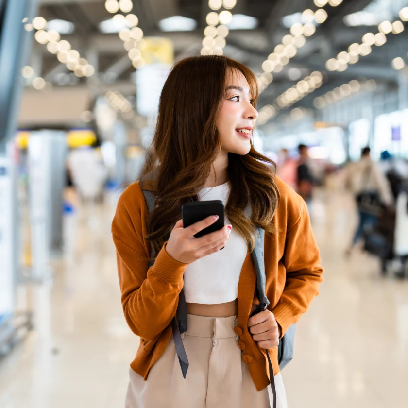 Traveller holding a smartphone in an airport terminal, representing travel marketing trends and mobile engagement.