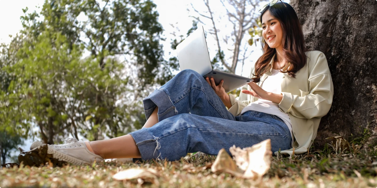 Person sitting outdoors by a tree using a laptop.