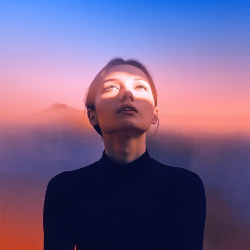 Person looking upward as warm light crosses their face against a pink and blue background.