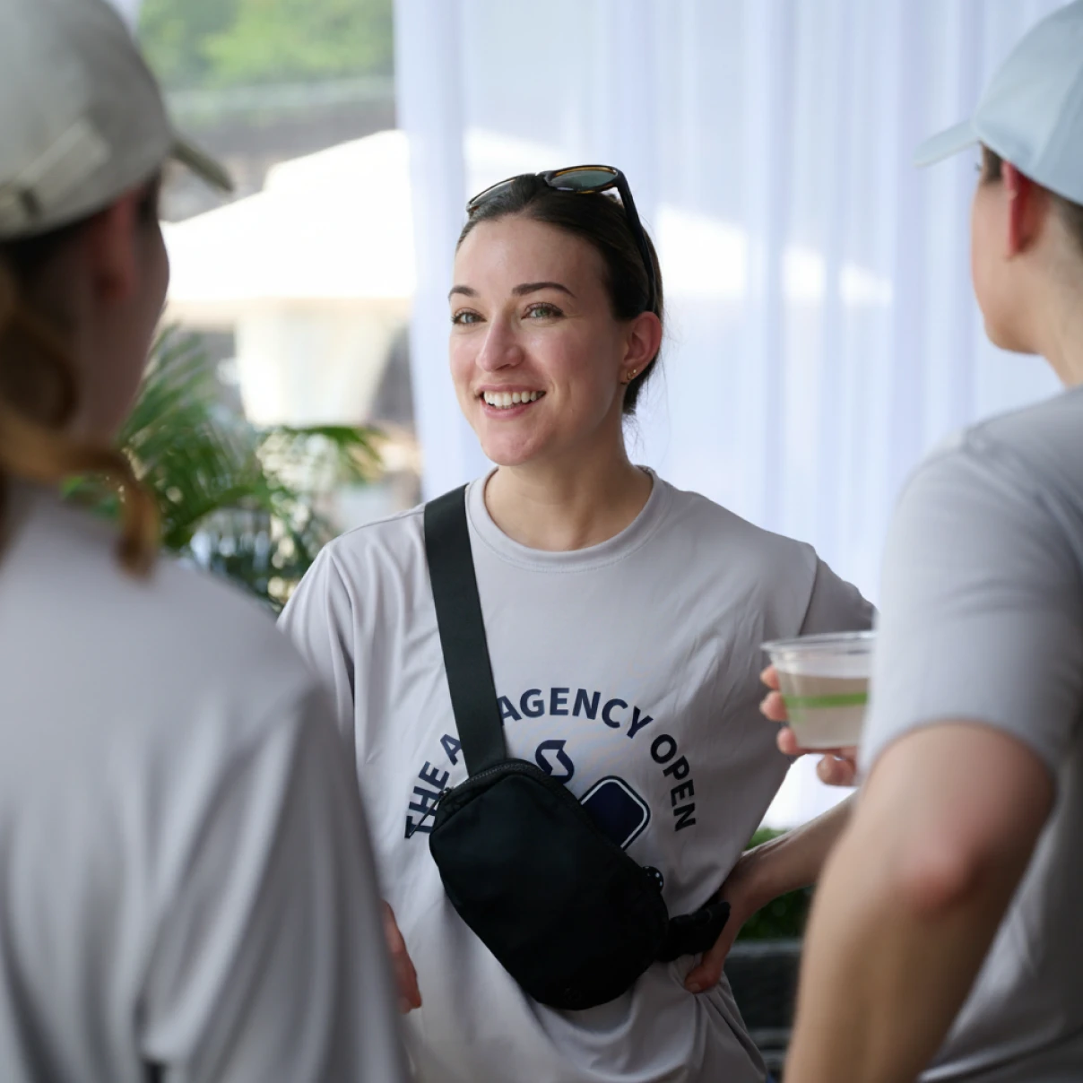 Person wearing an AdAgency Open t-shirt talking with two people in a bright indoor setting.