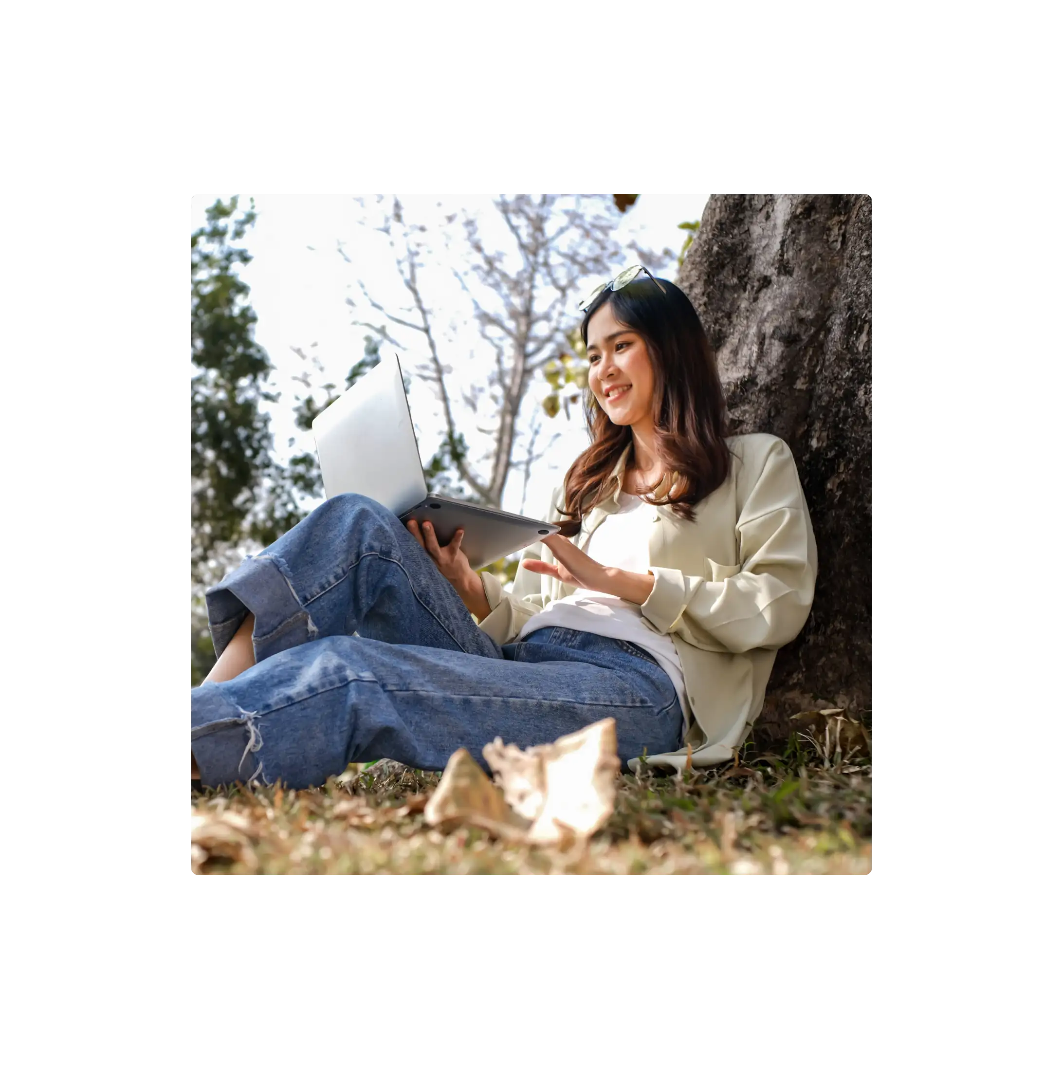 Person sitting outdoors by a tree using a laptop.